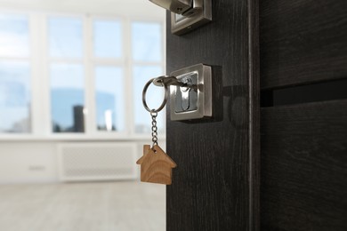 Photo of Open door with key and house shaped keychain, closeup. Space for text