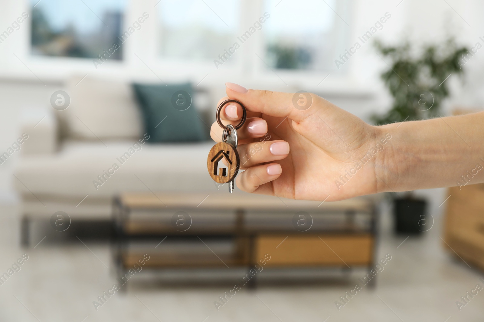 Photo of Woman holding key with house shaped keychain indoors, closeup