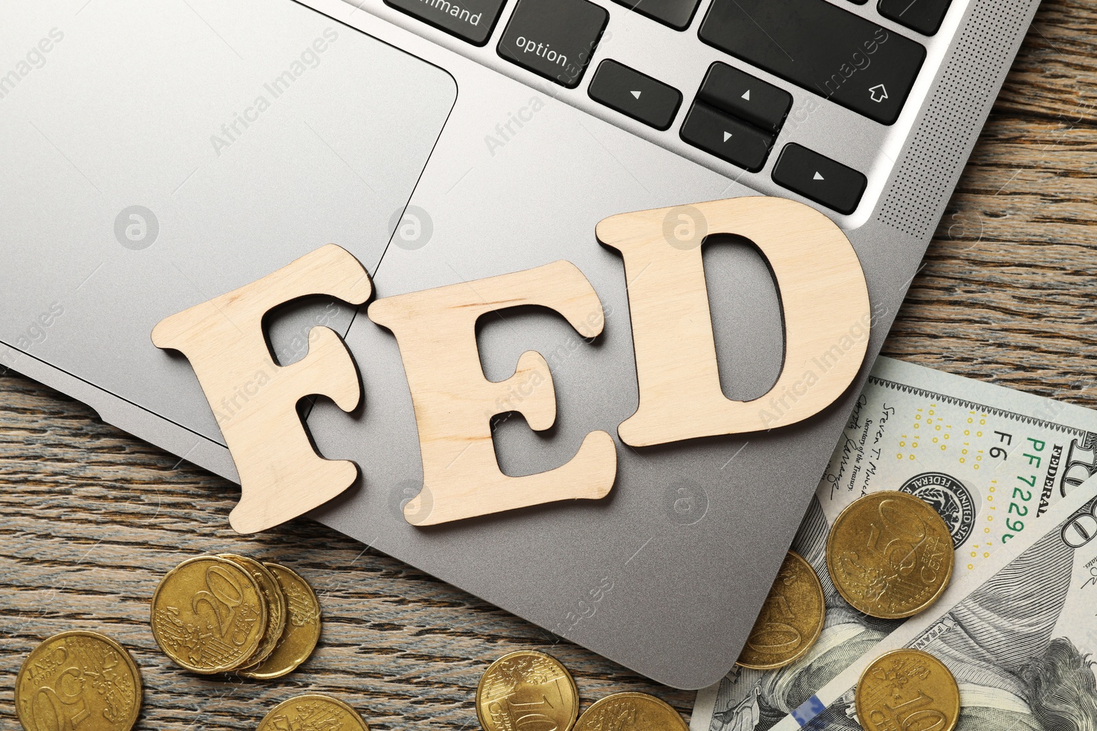 Photo of Letters Fed (Federal Reserve System), coins, dollar banknotes and laptop on wooden table, flat lay