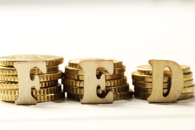 Photo of Wooden letters Fed (Federal Reserve System) and stacks of coins on white table, closeup