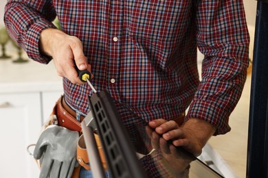 Photo of Repairman with screwdriver fixing oven indoors, closeup