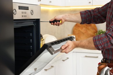 Repairman with screwdriver fixing oven in kitchen, closeup