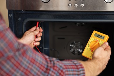 Photo of Repairman testing oven element with multimeter, closeup