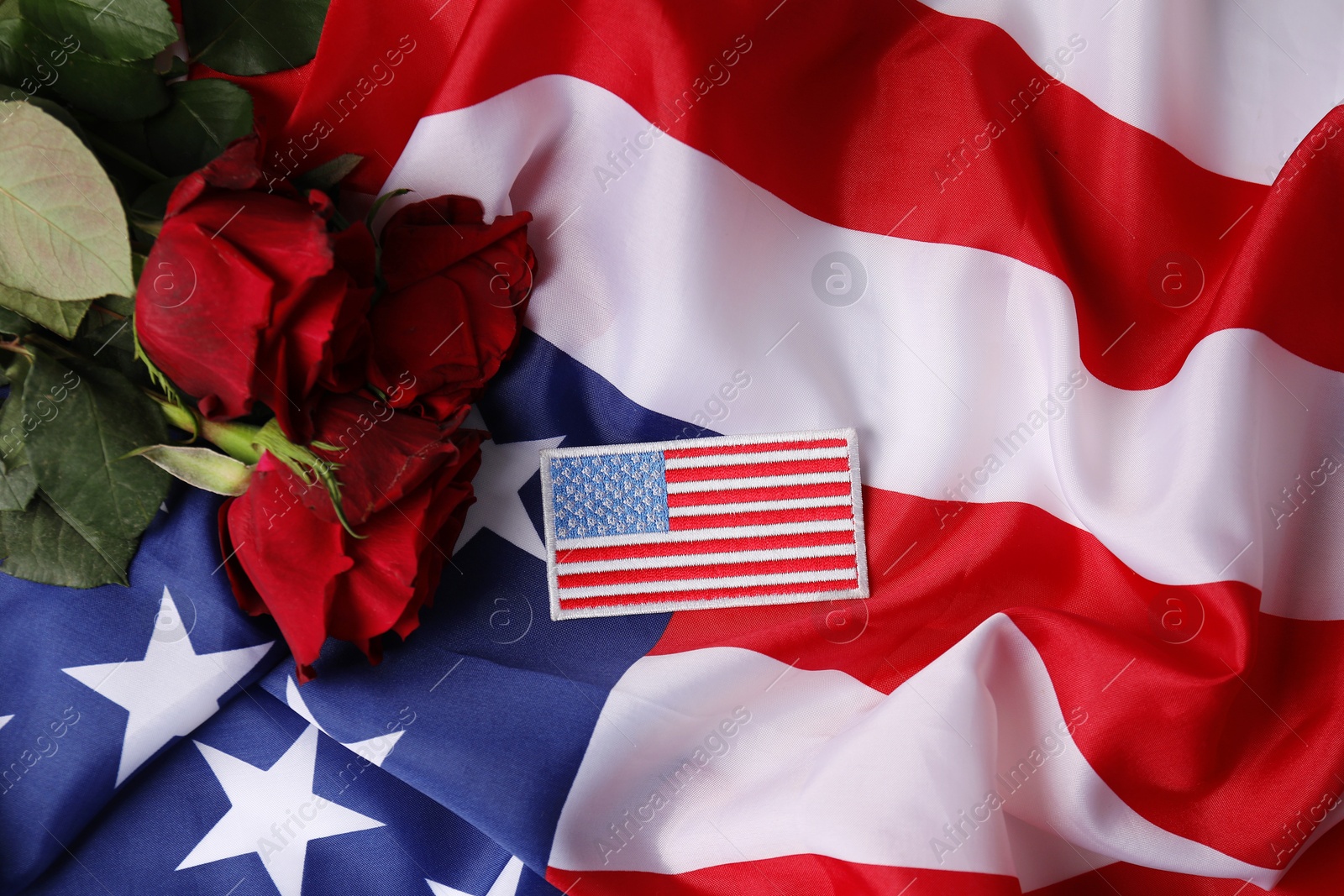 Photo of Veterans day. USA army patch and rose flowers on American flag, top view