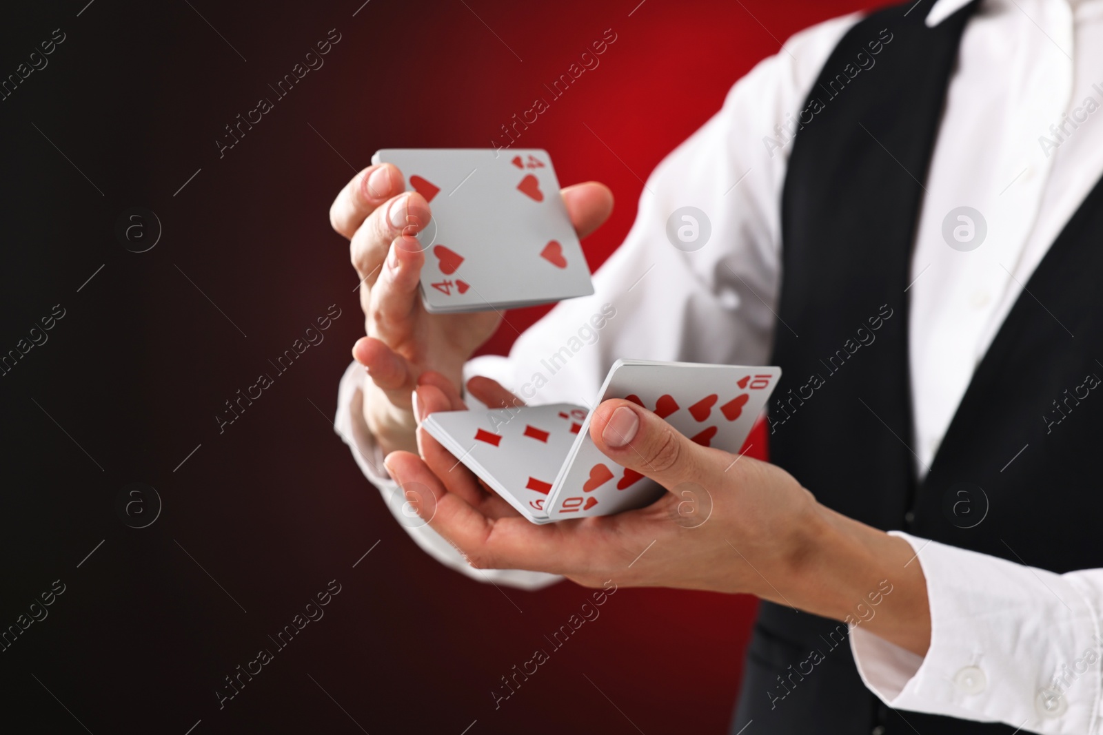 Photo of Professional croupier shuffling cards on dark red background, closeup