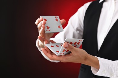 Photo of Professional croupier shuffling cards on dark red background, closeup