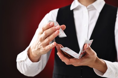 Professional croupier shuffling cards on dark red background, closeup