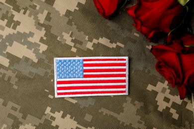 Photo of Veterans day. USA army patch and rose flowers on camouflage fabric, flat lay