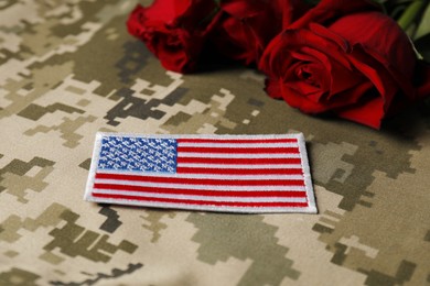 Photo of Veterans day. USA army patch and rose flowers on camouflage fabric, closeup