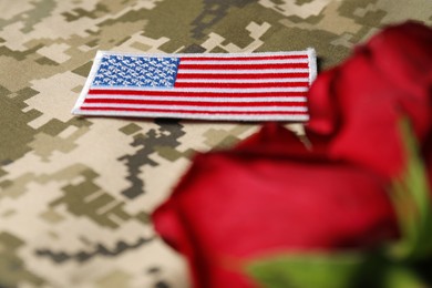 Photo of Veterans day. USA army patch and rose flowers on camouflage fabric, closeup