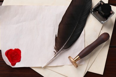 Photo of Old letter, wax stamps, feather, inkwell and envelopes on wooden table, top view