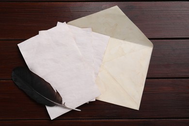 Photo of Old letters, envelope and feather on wooden table, top view