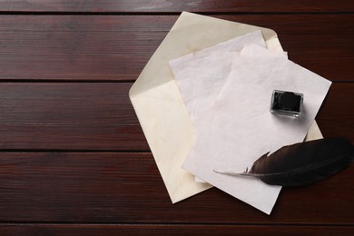 Photo of Old letters, envelope, feather and inkwell on wooden table, top view. Space for text