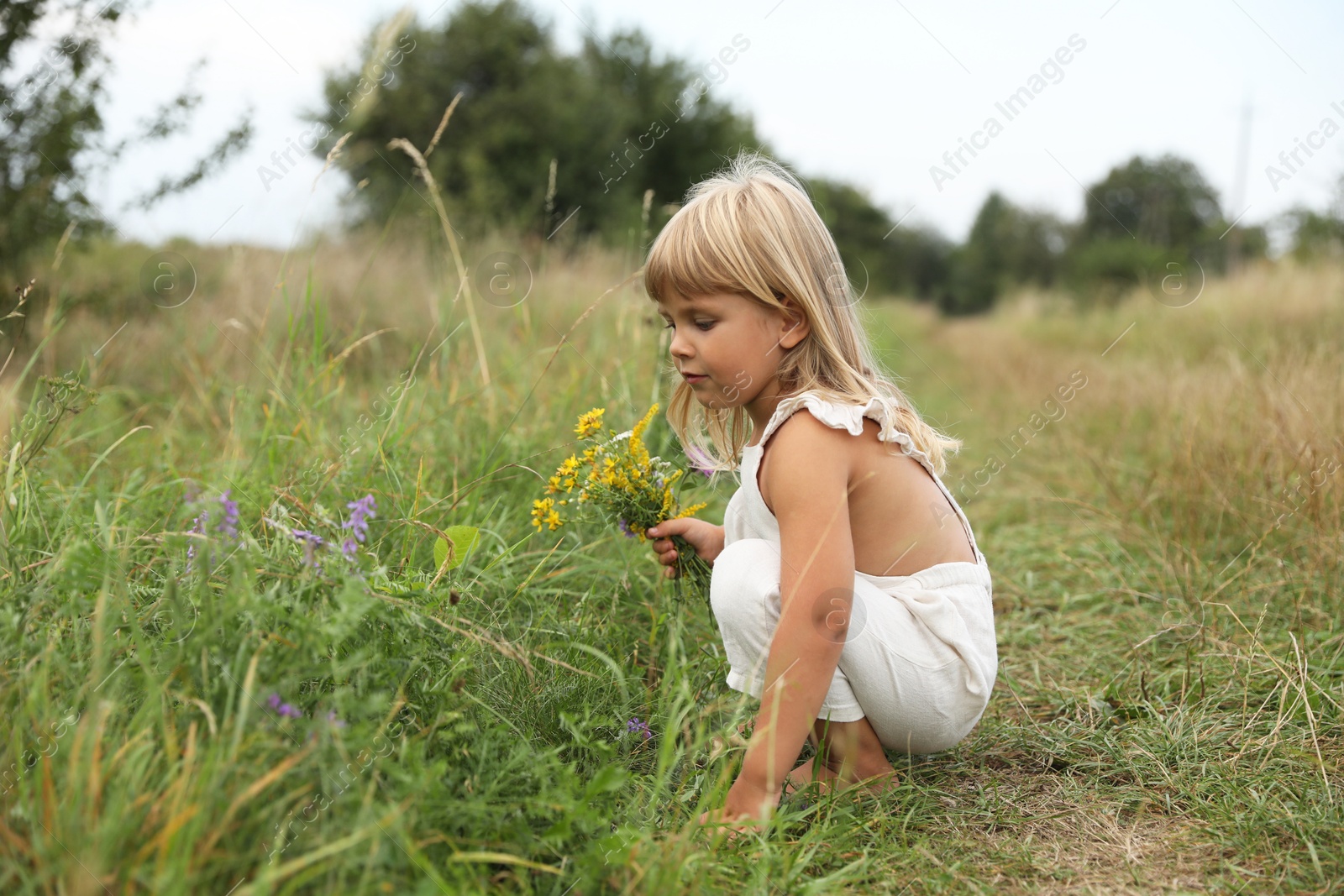 Photo of Cute little girl with flowers at meadow. Child enjoying beautiful nature