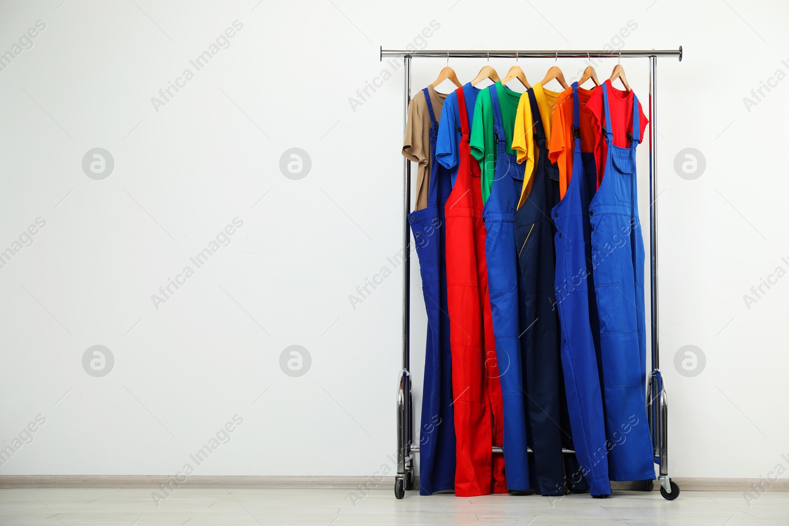 Photo of Workers' uniforms on clothing rack near grey wall indoors. Space for text