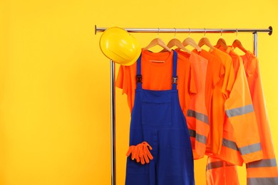 Photo of Workers' uniforms on clothing rack against yellow background. Space for text