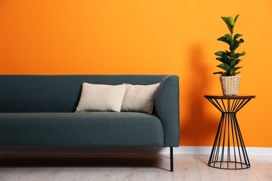 Photo of Stylish sofa with cushions and plant on side table near orange wall