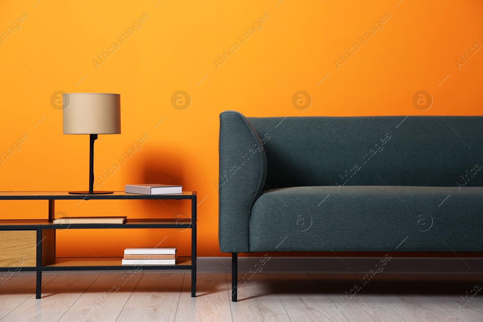 Photo of Stylish sofa and lamp with books on coffee table near orange wall