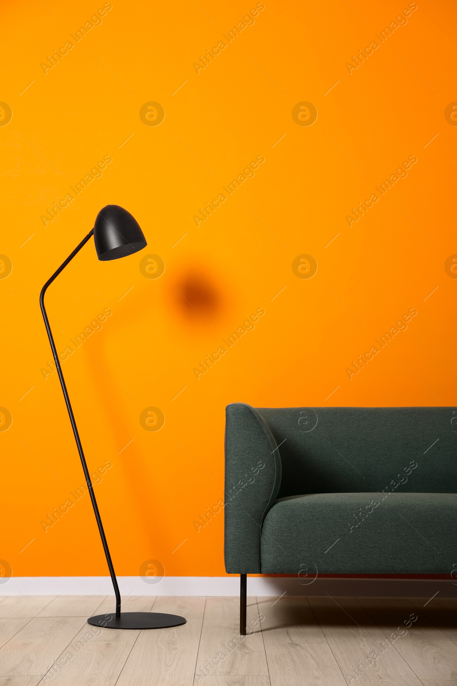 Photo of Stylish sofa and floor lamp near orange wall