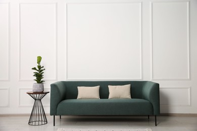 Photo of Stylish sofa with cushions and plant on side table near white wall