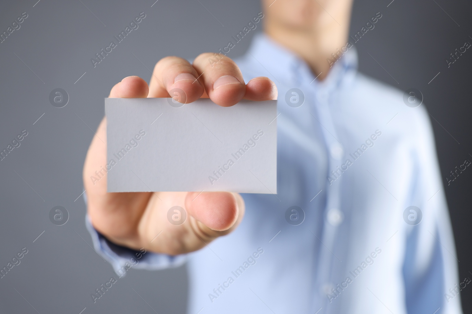 Photo of Man holding blank business card on grey background, closeup. Mockup for design