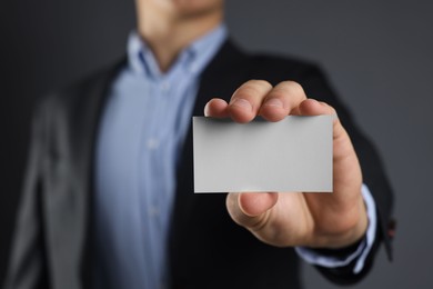 Man holding blank business card on grey background, closeup. Mockup for design