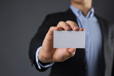 Man holding blank business card on grey background, closeup. Mockup for design