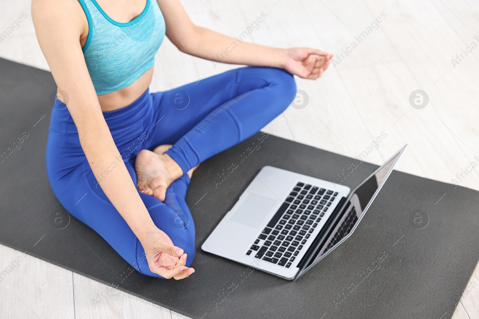 Photo of Woman meditating near laptop on yoga mat at home, closeup