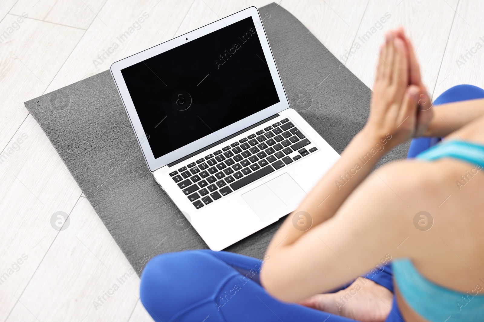 Photo of Woman meditating near laptop on yoga mat at home, closeup