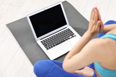 Woman meditating near laptop on yoga mat at home, closeup