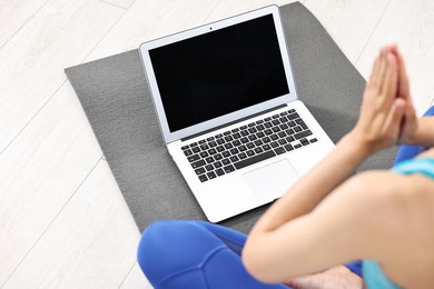 Woman meditating near laptop on yoga mat at home, closeup