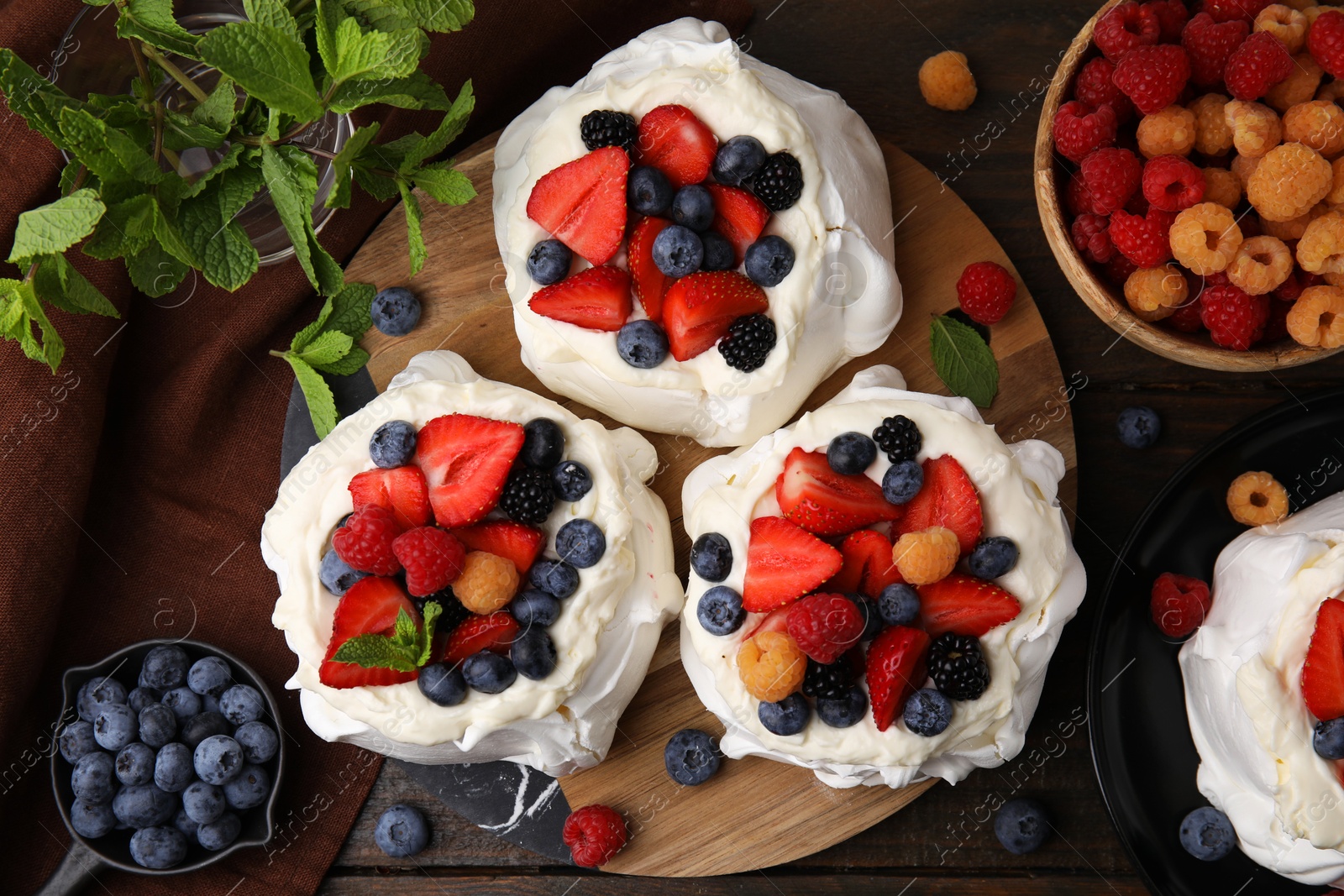 Photo of Pavlova cake (meringue dessert) with whipped cream, fresh berries and mint on wooden table, flat lay