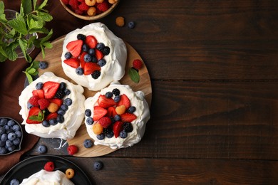 Photo of Pavlova cake (meringue dessert) with whipped cream, fresh berries and mint on wooden table, flat lay. Space for text