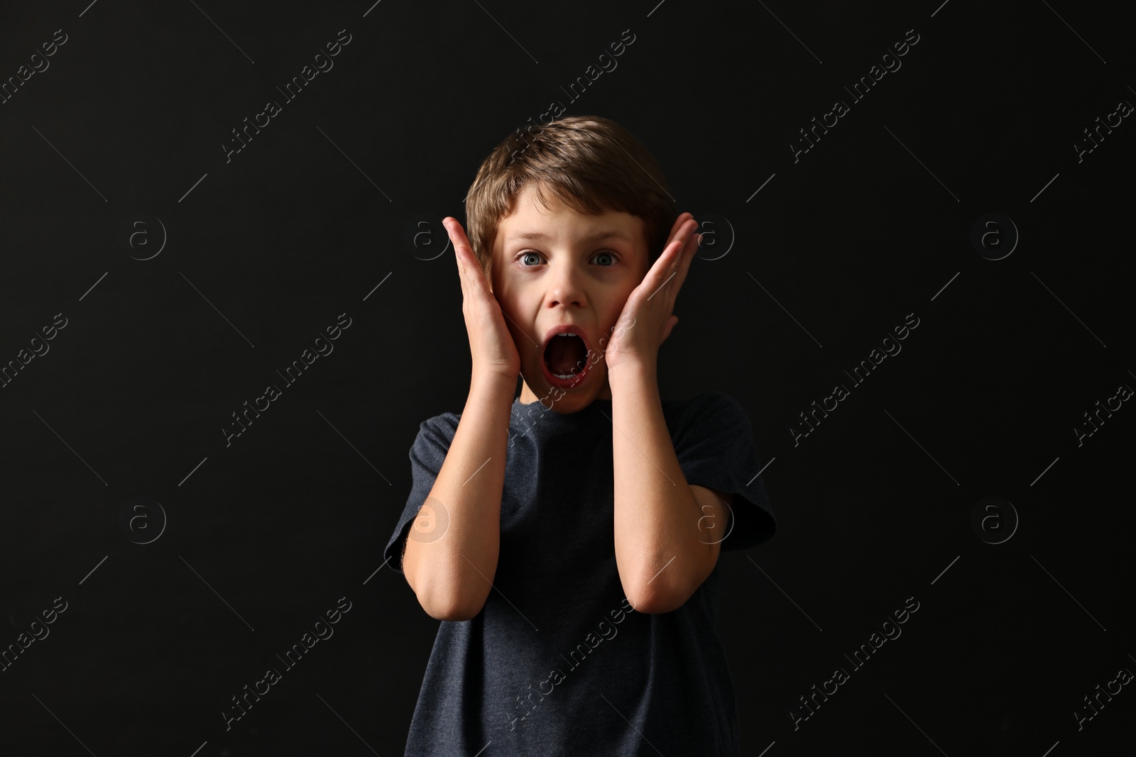 Photo of Scared little boy screaming on black background