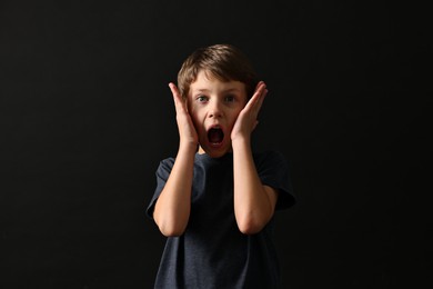 Photo of Scared little boy screaming on black background