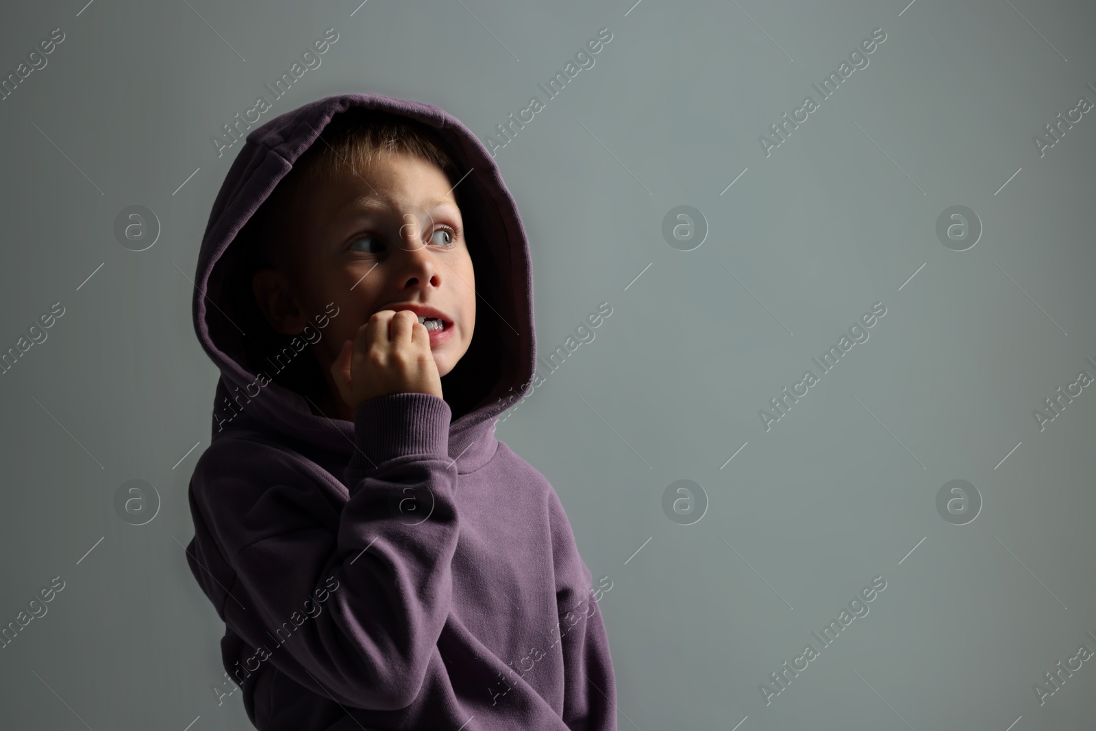 Photo of Scared little boy on grey background. Space for text