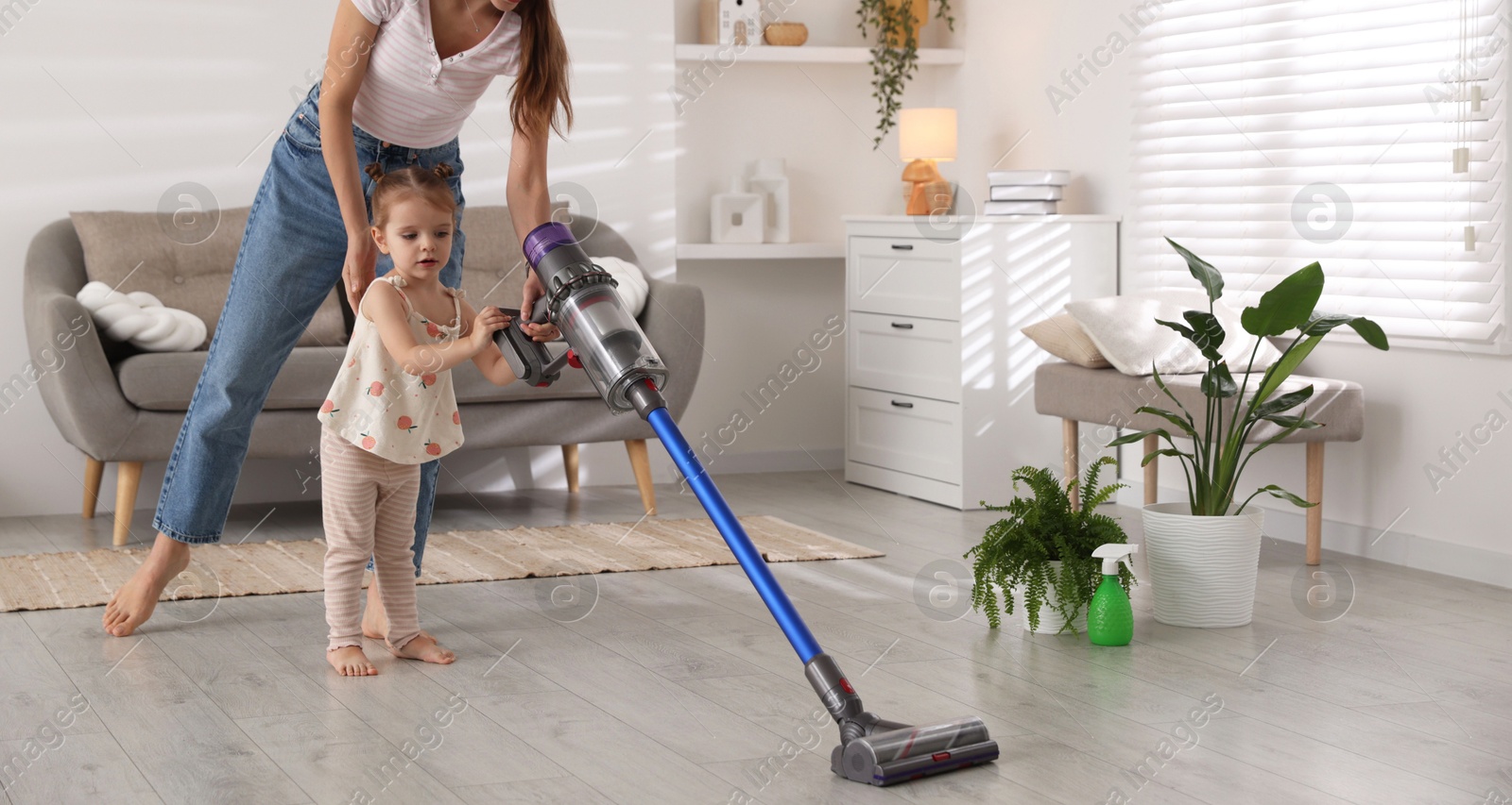 Photo of Young woman and her daughter cleaning floor with cordless vacuum cleaner at home, closeup