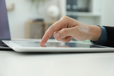 Photo of Businesswoman using tablet at white table indoors, closeup. Modern technology