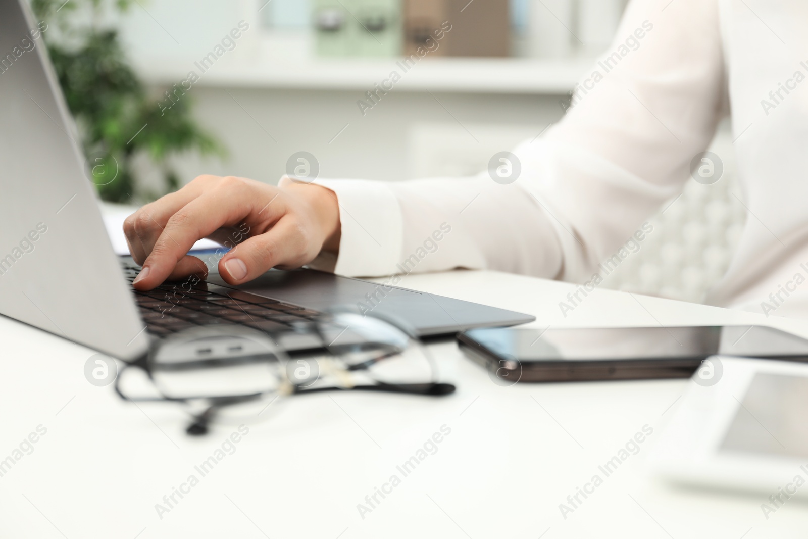 Photo of Businesswoman using laptop at white table indoors, closeup. Modern technology