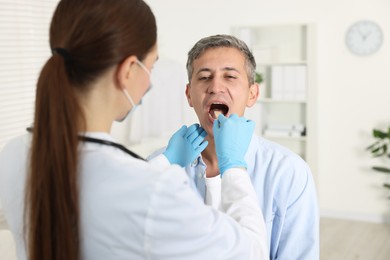 Doctor examining man's throat with tongue depressor in clinic