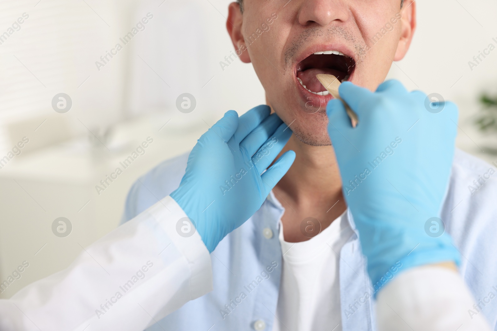 Photo of Doctor examining man's throat with tongue depressor in clinic, closeup