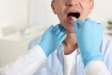 Doctor examining man's throat with tongue depressor in clinic, closeup