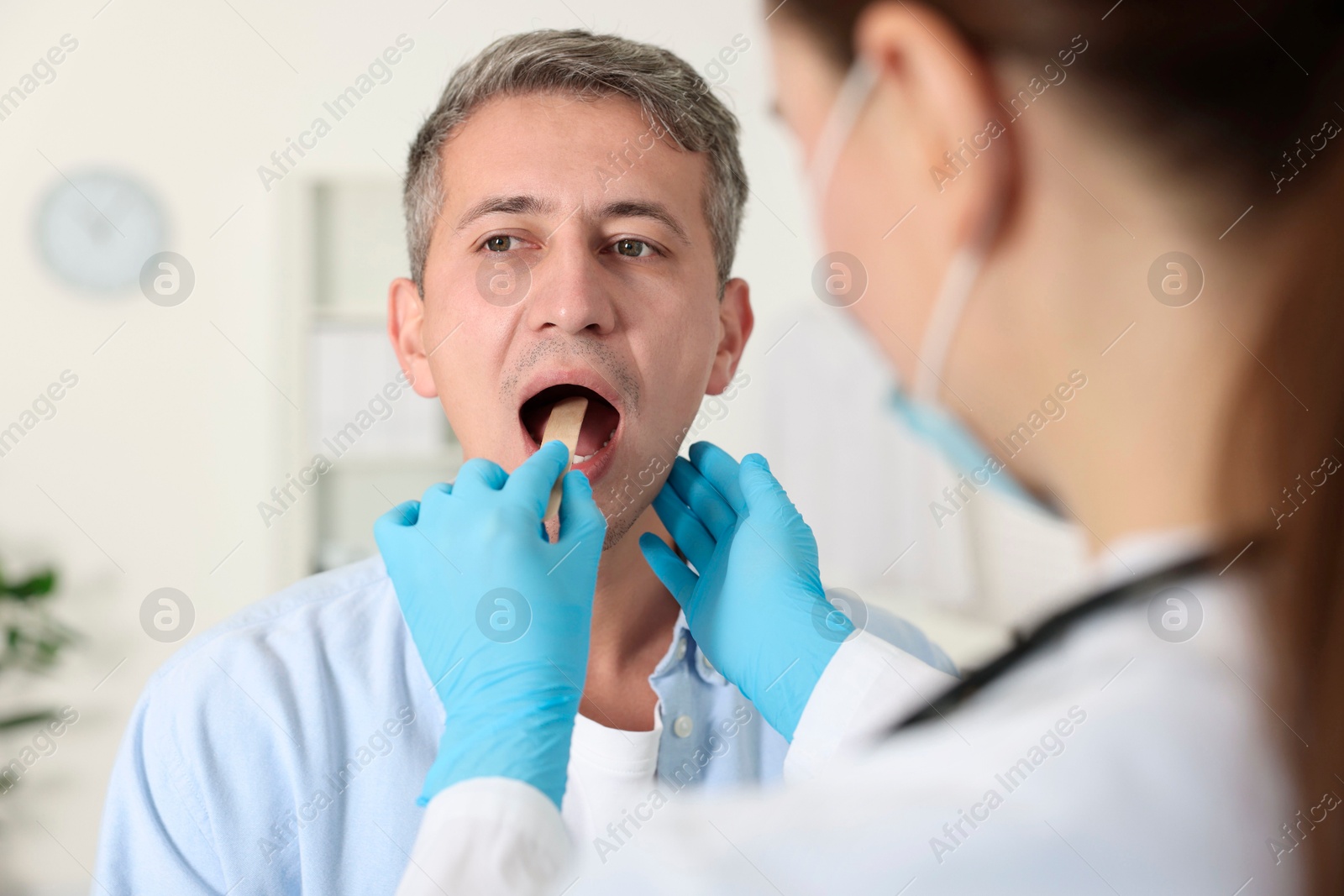 Photo of Doctor examining man's throat with tongue depressor in clinic