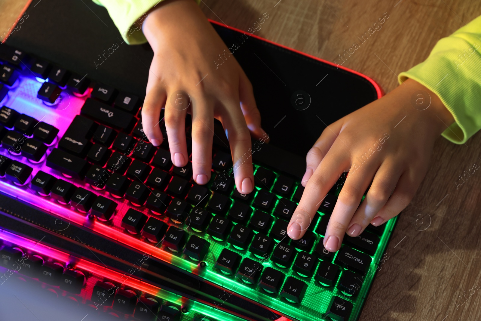 Photo of Girl using computer keyboard at wooden table, top view