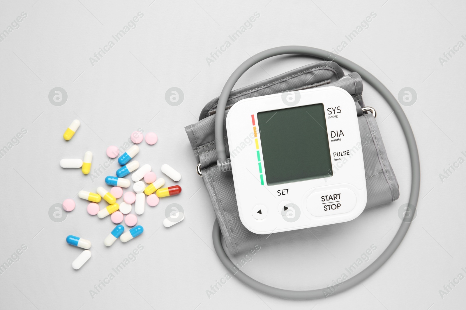 Photo of Blood pressure measuring device and pills on light grey background, top view