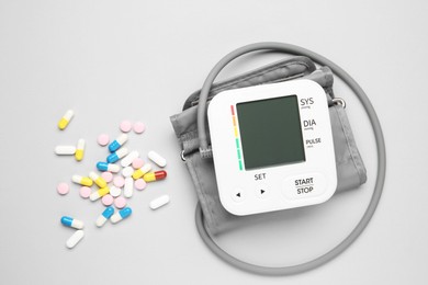 Photo of Blood pressure measuring device and pills on light grey background, top view