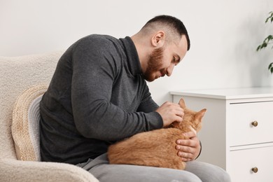 Photo of Man petting cute ginger cat on armchair at home