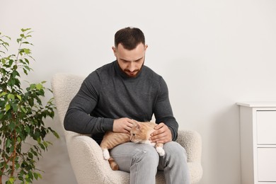 Man petting cute ginger cat on armchair at home