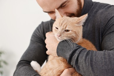 Photo of Man petting cute ginger cat at home, closeup