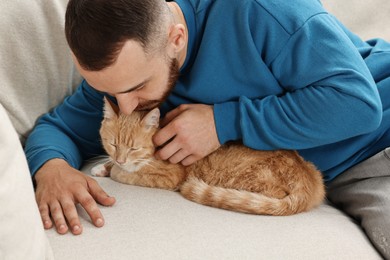 Photo of Man petting cute ginger cat on sofa at home